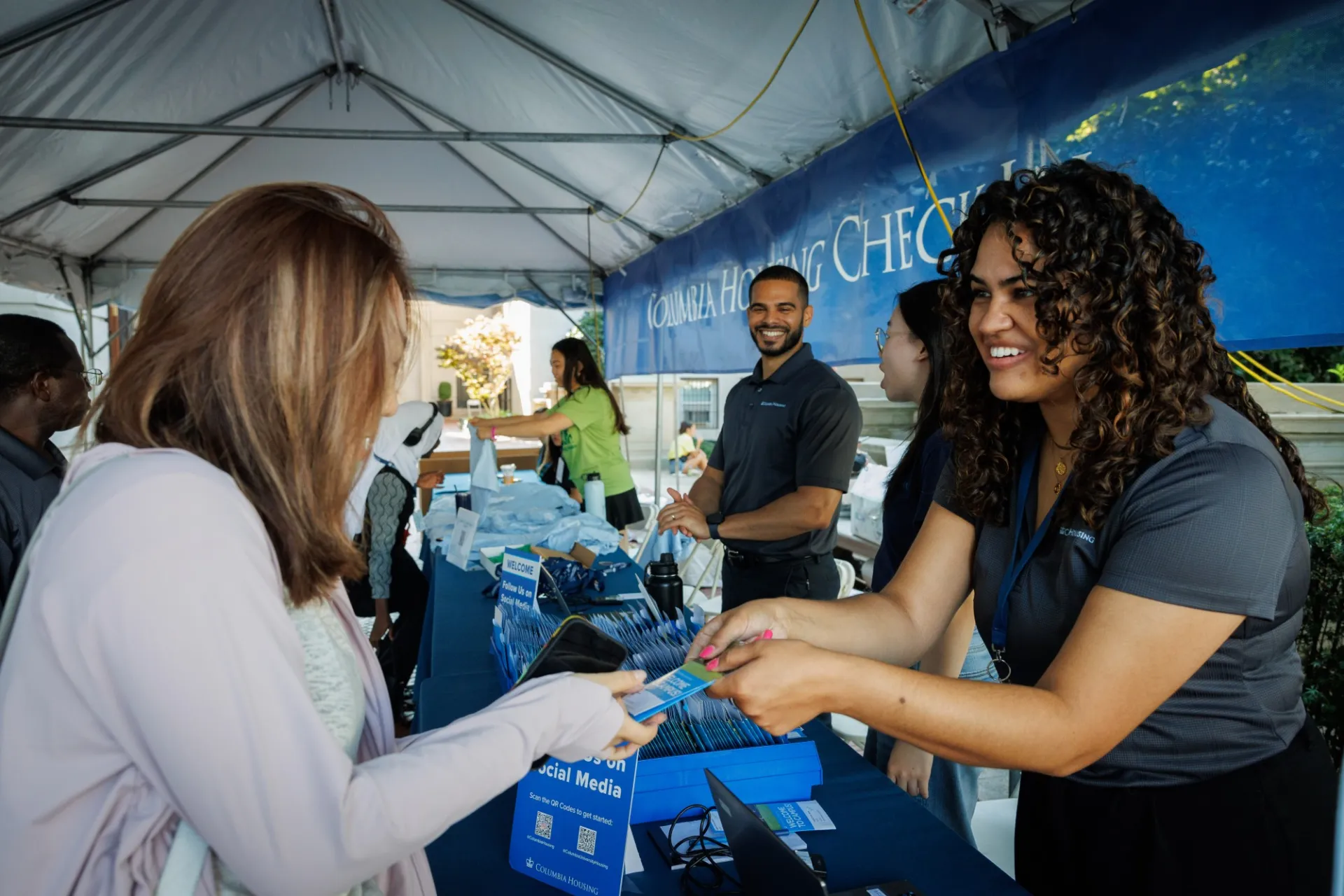 A Columbia Housing team member hands a brochure to a student at the Housing Check-in tent.