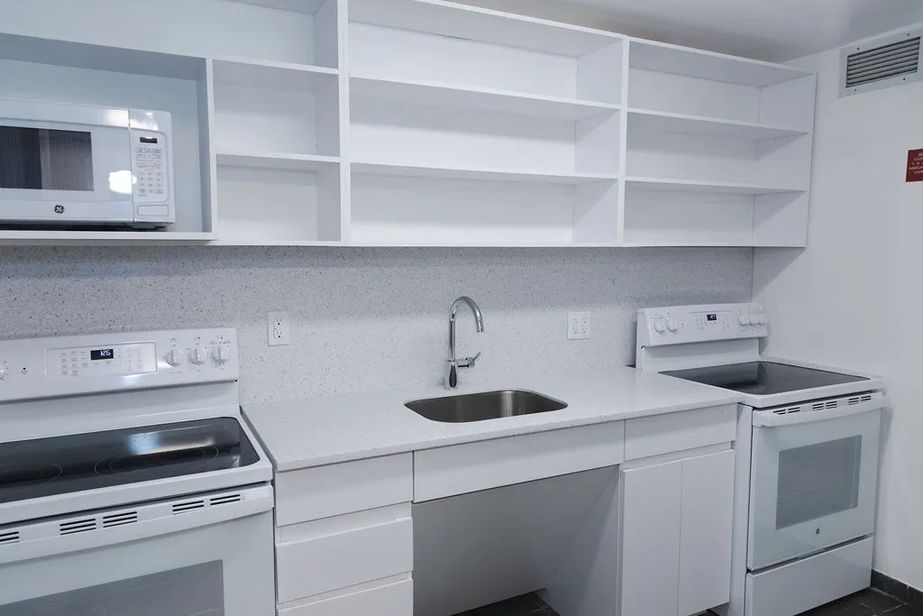 A kitchen in Broadway Hall that has white shelving, cabinets, and appliances.