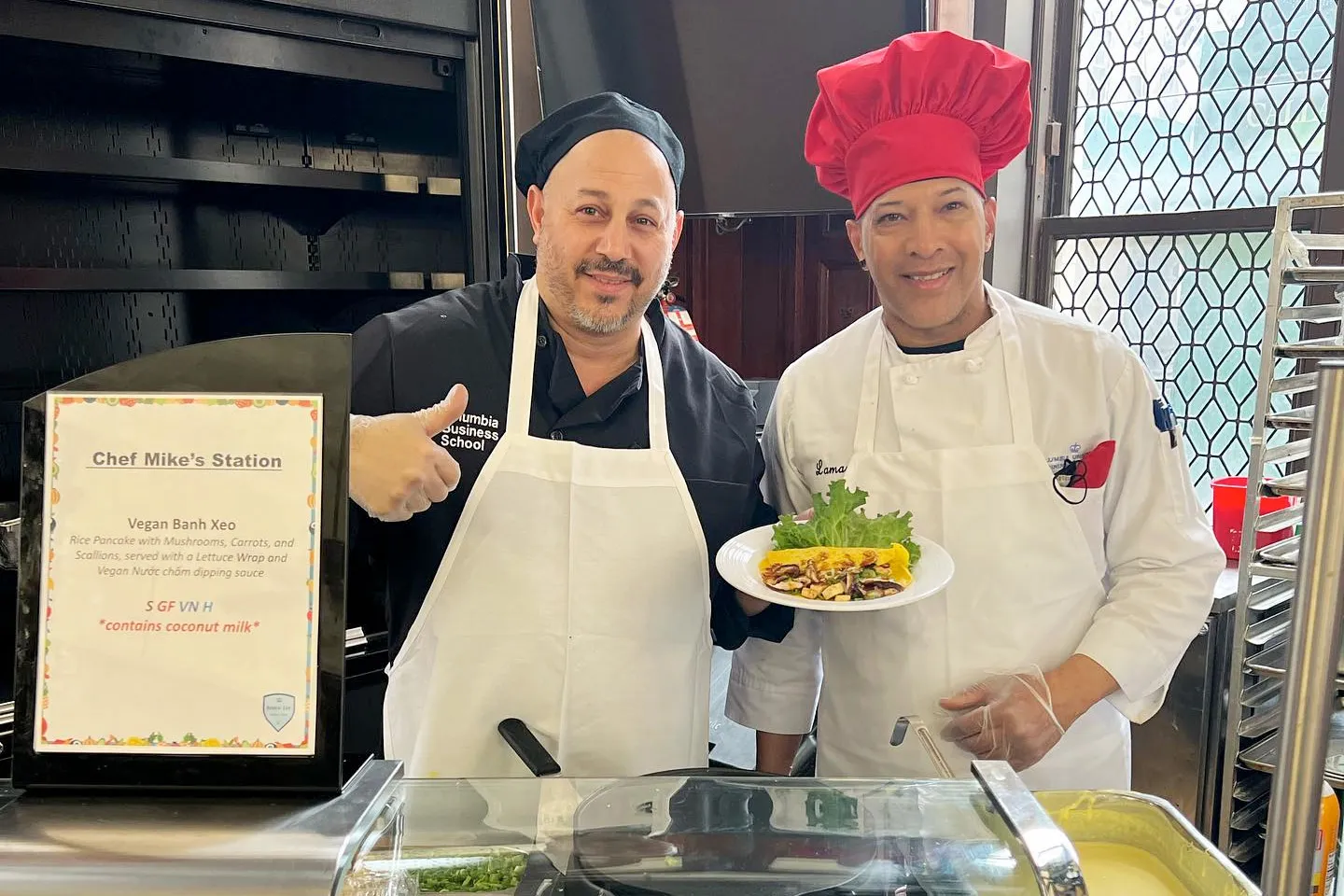Two chefs hold up a Vegan Banh Xeo dish at Chef Mike's Station in John Jay Hall.