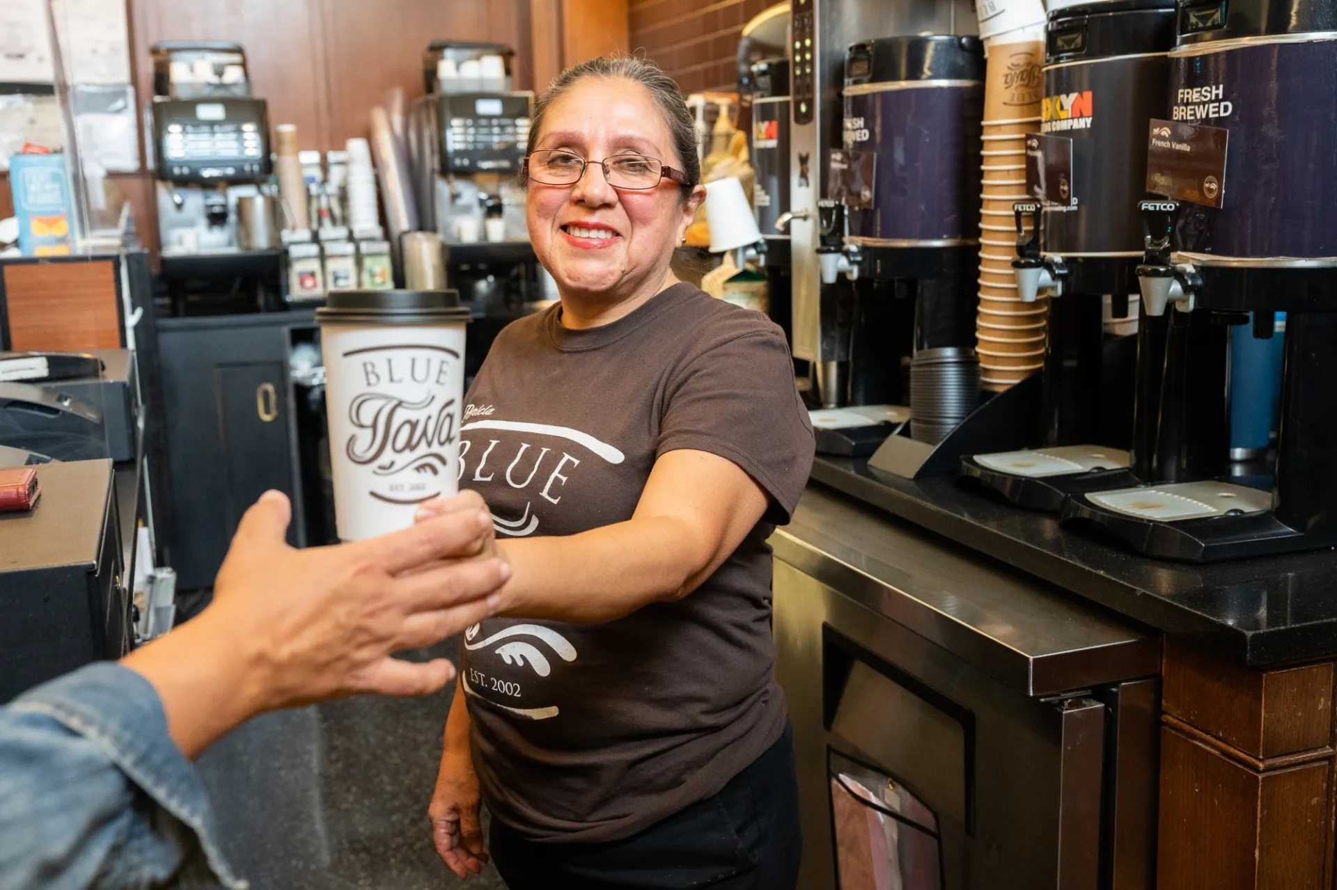 A Blue Java employee smiles and hands out a cup of coffee to a customer.