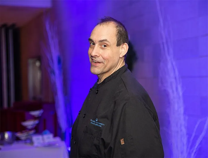 Chef Donald Bartlett looking at the camera in front of a purple lit wall.