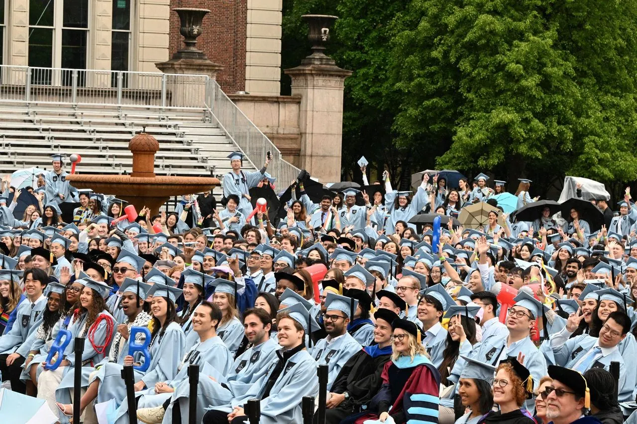 A group of students and staff dressed in regalia gather in Low Plaza for convocation.