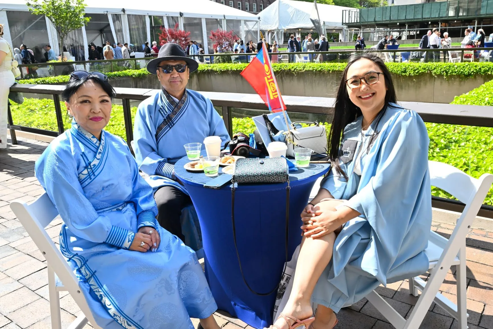 A graduate sits with her parents at a table with food and drinks. 