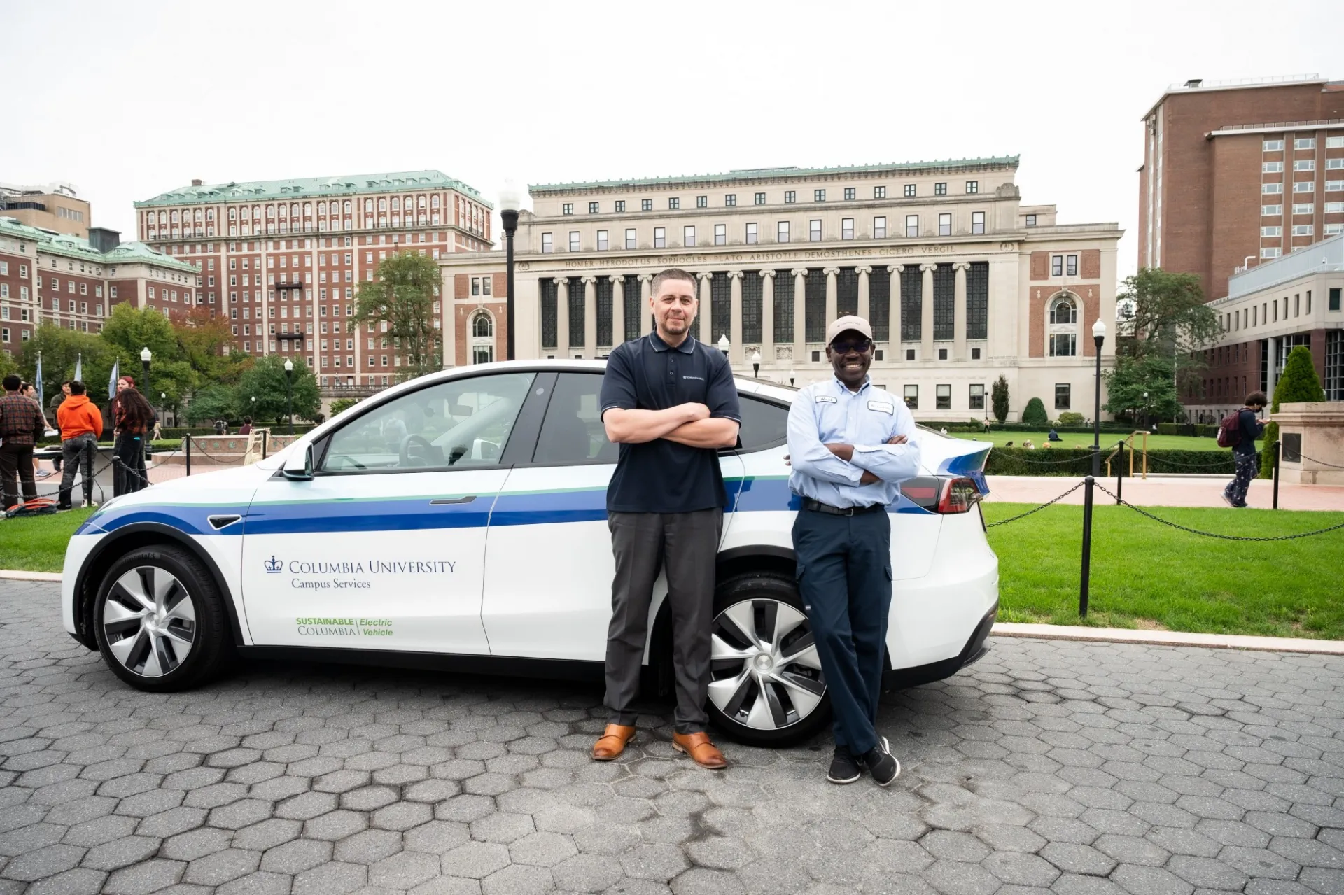 David Ramos stands next to another Columbia Mail worker in front of a Campus Services car.