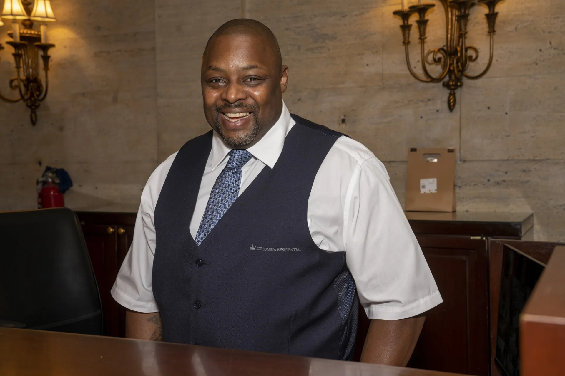 A Columbia Residential doorman poses for the camera from behind the receptionist desk.